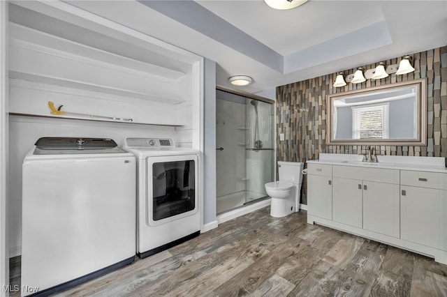 interior space featuring hardwood / wood-style floors, vanity, a shower with door, washer and dryer, and toilet