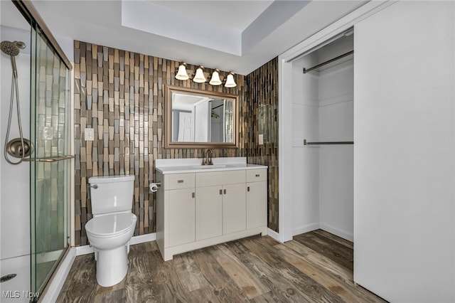 bathroom with vanity, hardwood / wood-style flooring, toilet, tile walls, and a shower with shower door