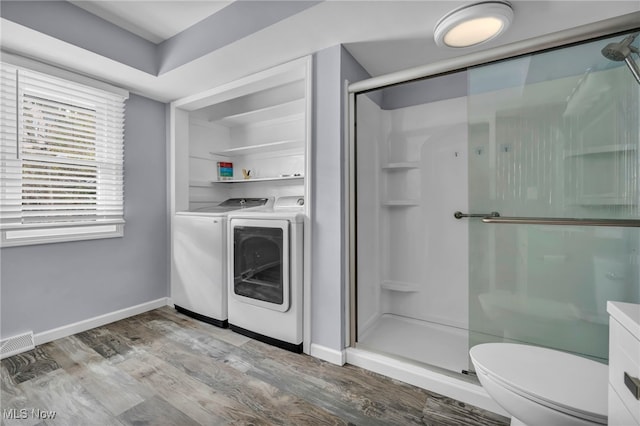 bathroom with hardwood / wood-style flooring, toilet, independent washer and dryer, and a shower with door