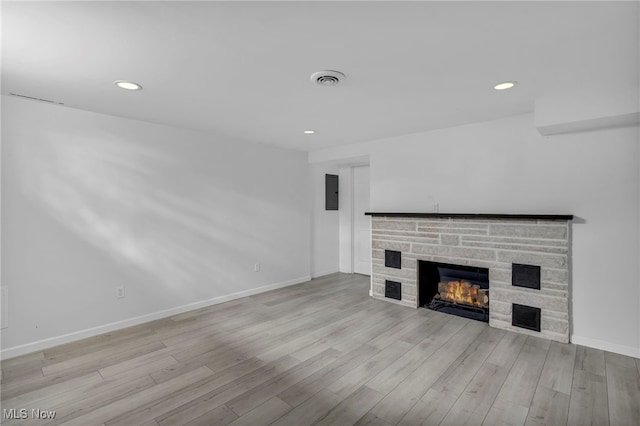 unfurnished living room with a stone fireplace, light hardwood / wood-style flooring, and electric panel