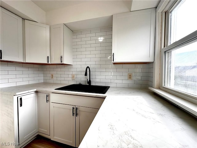 kitchen featuring decorative backsplash, light stone counters, white cabinetry, and sink