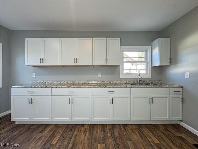 kitchen featuring light stone countertops, dark hardwood / wood-style floors, white cabinetry, and sink