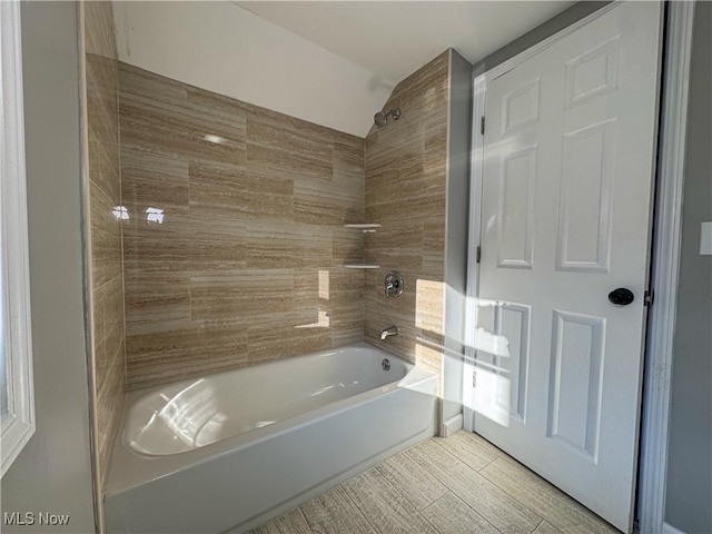 bathroom with tiled shower / bath combo and lofted ceiling