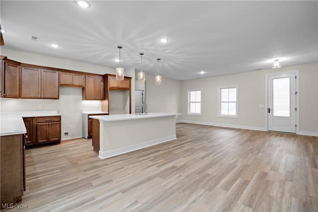 kitchen with decorative light fixtures, light hardwood / wood-style floors, and a kitchen island with sink