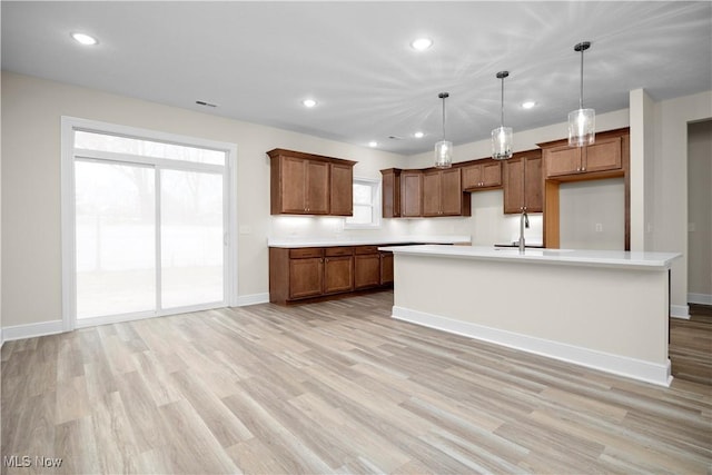 kitchen featuring light wood-type flooring, decorative light fixtures, plenty of natural light, and a kitchen island with sink