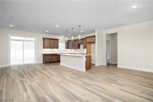 kitchen featuring a center island with sink, light hardwood / wood-style flooring, hanging light fixtures, and a healthy amount of sunlight