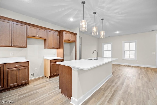 kitchen featuring sink, light wood-type flooring, an island with sink, and hanging light fixtures