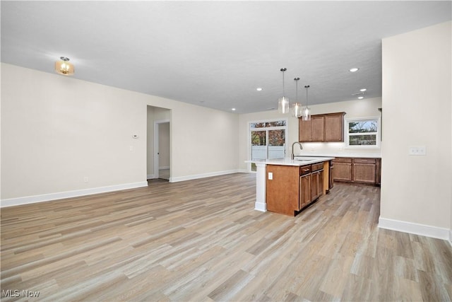 kitchen featuring decorative light fixtures, sink, light wood-type flooring, and an island with sink