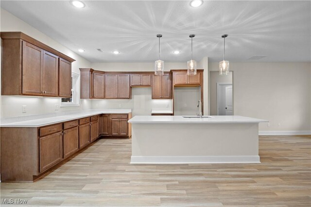 kitchen featuring pendant lighting, a center island with sink, light hardwood / wood-style flooring, and sink