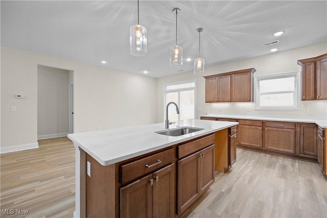 kitchen featuring hanging light fixtures, sink, light hardwood / wood-style floors, and a center island with sink