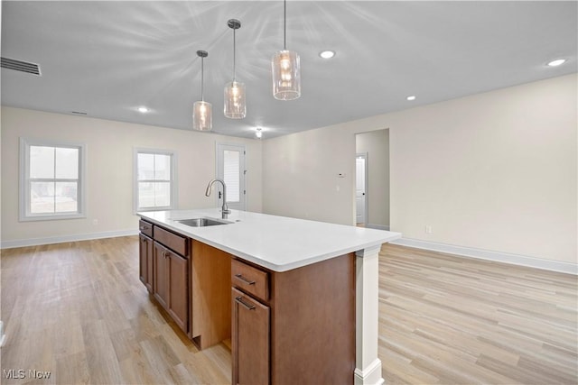 kitchen featuring light hardwood / wood-style floors, sink, hanging light fixtures, and a kitchen island with sink