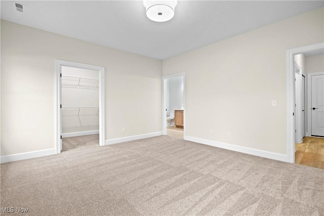 unfurnished bedroom with a spacious closet, a closet, and light colored carpet