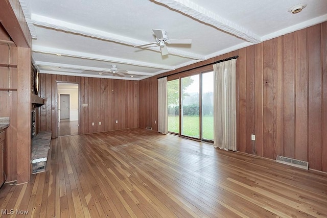 unfurnished room with beam ceiling, hardwood / wood-style flooring, ceiling fan, and wood walls