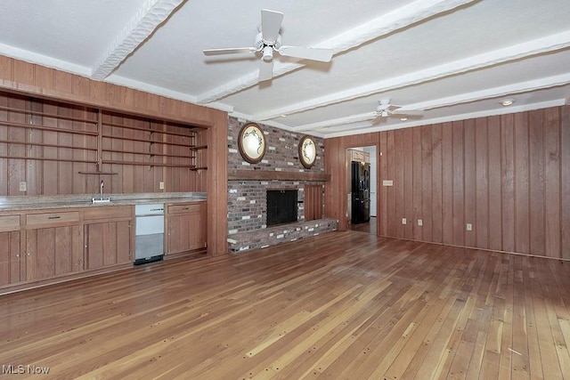 unfurnished living room featuring wooden walls, a fireplace, beamed ceiling, and light hardwood / wood-style floors