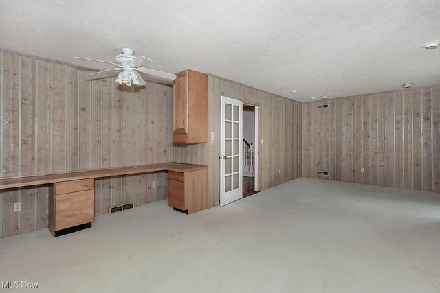 interior space featuring french doors, built in desk, ceiling fan, and wood walls