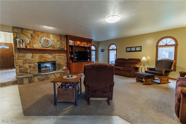 living room with a stone fireplace, plenty of natural light, a textured ceiling, and light wood-type flooring