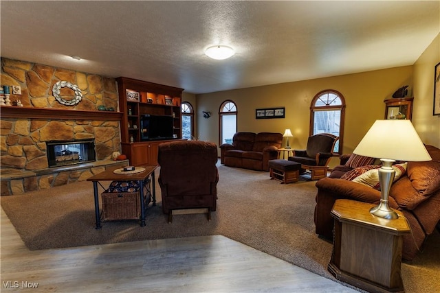 living room featuring a textured ceiling, light hardwood / wood-style floors, and a stone fireplace