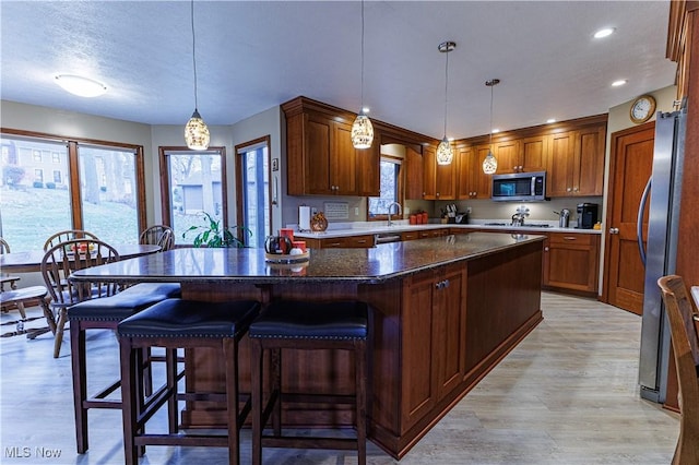 kitchen with a kitchen breakfast bar, appliances with stainless steel finishes, pendant lighting, a kitchen island, and light wood-type flooring