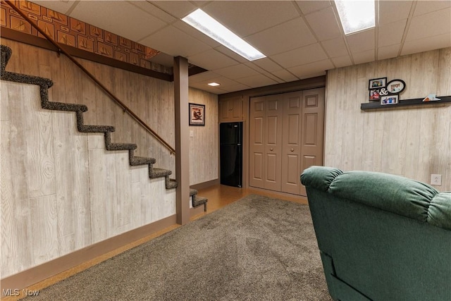 interior space featuring a paneled ceiling, carpet floors, black fridge, and wooden walls