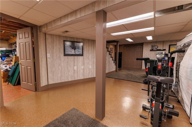 workout area with a drop ceiling and wooden walls