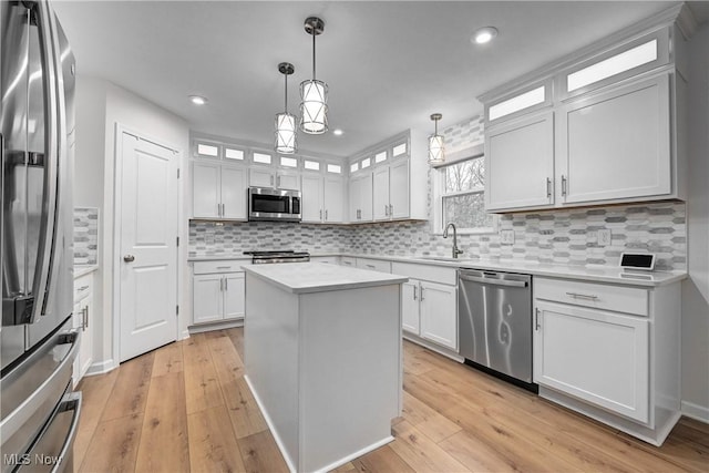 kitchen featuring sink, stainless steel appliances, a kitchen island, pendant lighting, and white cabinets