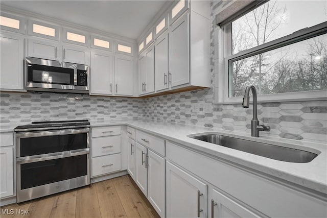 kitchen featuring white cabinets, sink, light hardwood / wood-style flooring, decorative backsplash, and stainless steel appliances