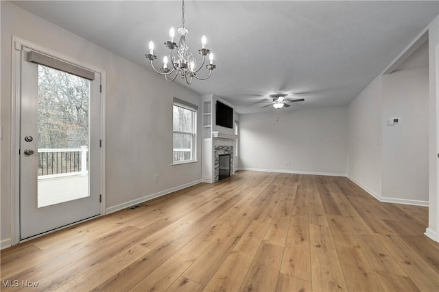 unfurnished living room with plenty of natural light, a fireplace, light hardwood / wood-style floors, and ceiling fan with notable chandelier