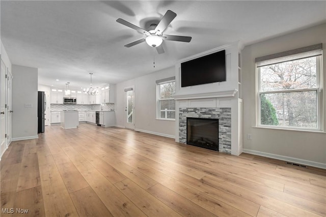 unfurnished living room featuring a fireplace, ceiling fan with notable chandelier, and light hardwood / wood-style flooring