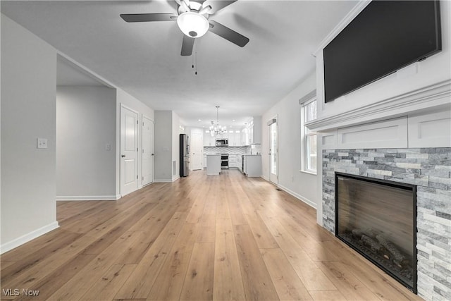 unfurnished living room with a stone fireplace, light hardwood / wood-style flooring, and ceiling fan with notable chandelier