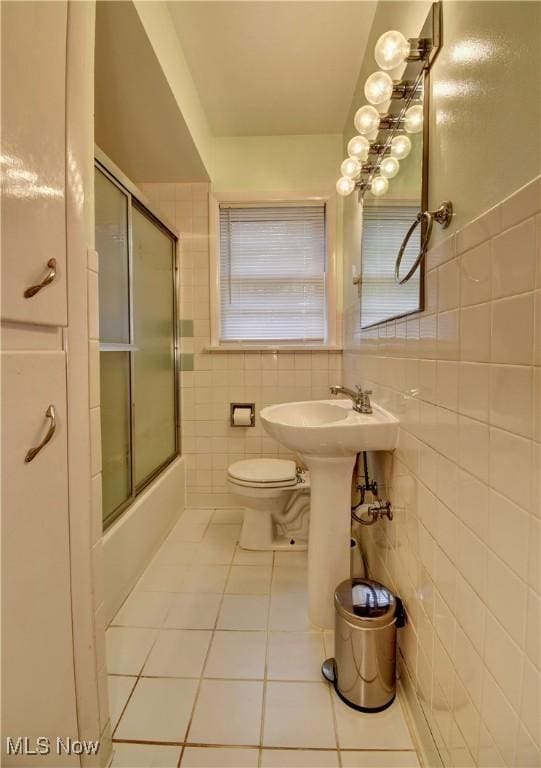 bathroom featuring toilet, tile patterned floors, tile walls, and bath / shower combo with glass door