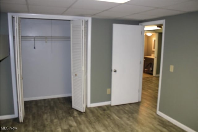 unfurnished bedroom with a closet, a drop ceiling, and dark wood-type flooring