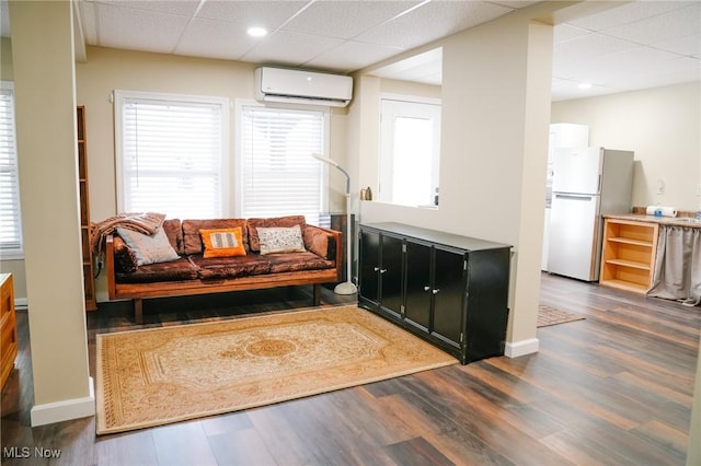 living room with a wall mounted AC, a drop ceiling, and dark hardwood / wood-style floors