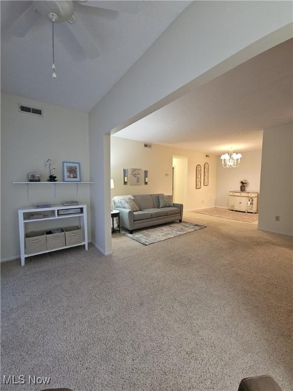 carpeted living room featuring ceiling fan with notable chandelier