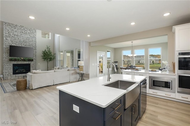 kitchen featuring stainless steel appliances, an inviting chandelier, an island with sink, white cabinets, and light wood-type flooring