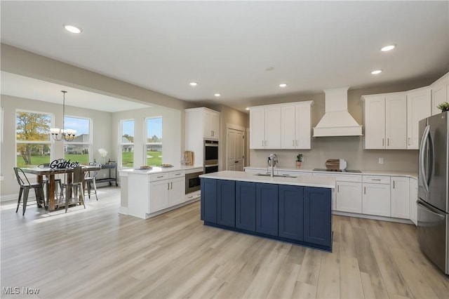 kitchen featuring a center island with sink, decorative light fixtures, custom range hood, and stainless steel appliances