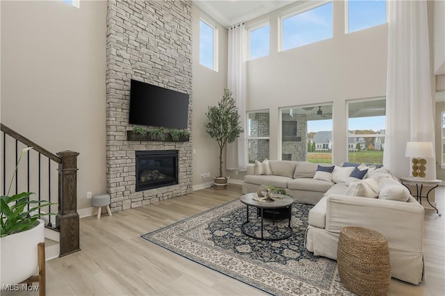 living room with a stone fireplace, a high ceiling, and light hardwood / wood-style flooring