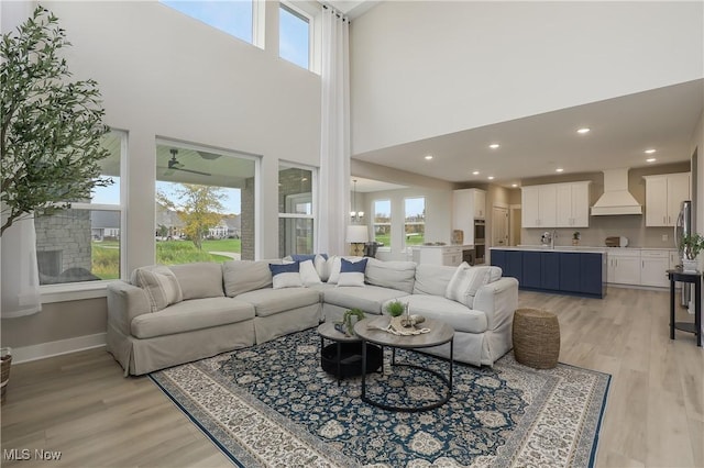 living room featuring ceiling fan, sink, light hardwood / wood-style floors, and a high ceiling