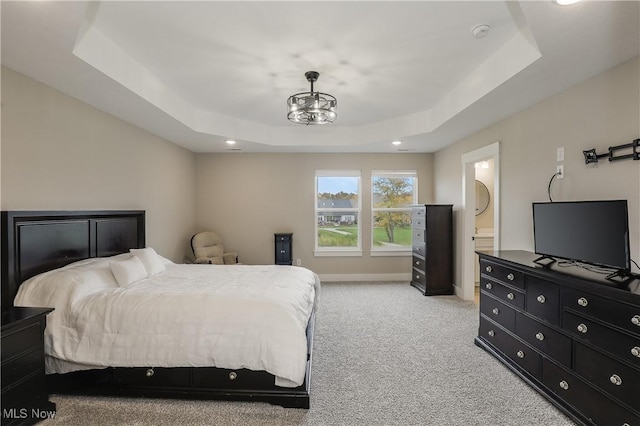 bedroom with a raised ceiling, light colored carpet, and ensuite bath