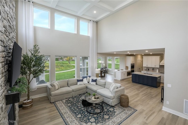 living room featuring a towering ceiling, coffered ceiling, sink, light hardwood / wood-style flooring, and beamed ceiling