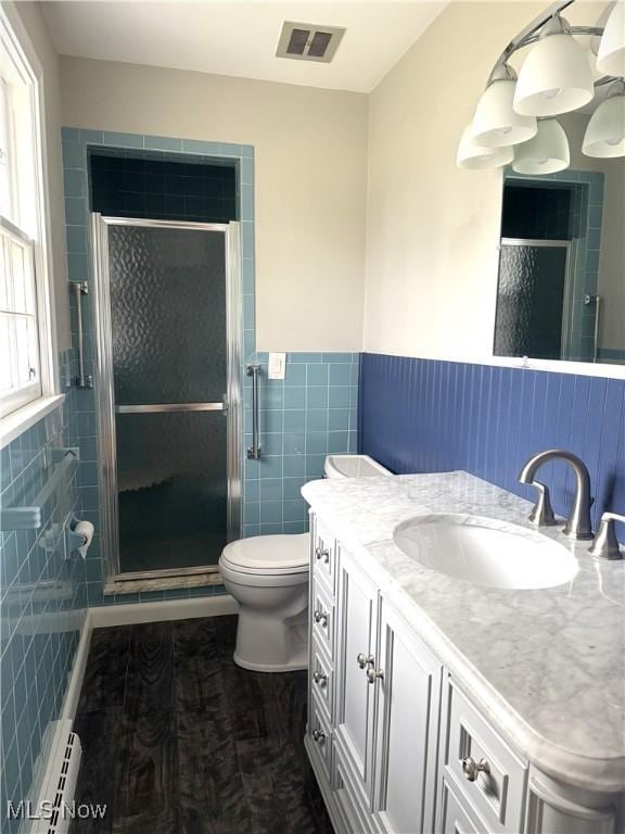 bathroom with baseboard heating, a shower with door, vanity, and tile walls