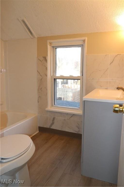 bathroom featuring a textured ceiling, toilet, vanity, tile walls, and hardwood / wood-style flooring