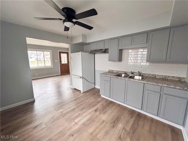 kitchen with sink, decorative backsplash, gray cabinets, light wood-type flooring, and white fridge