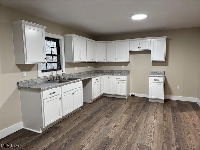 kitchen featuring light stone countertops, dark hardwood / wood-style flooring, white cabinetry, and sink