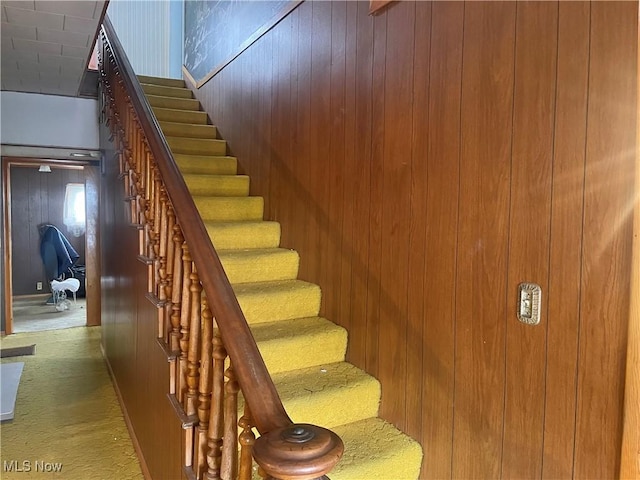 staircase featuring wooden walls and carpet floors