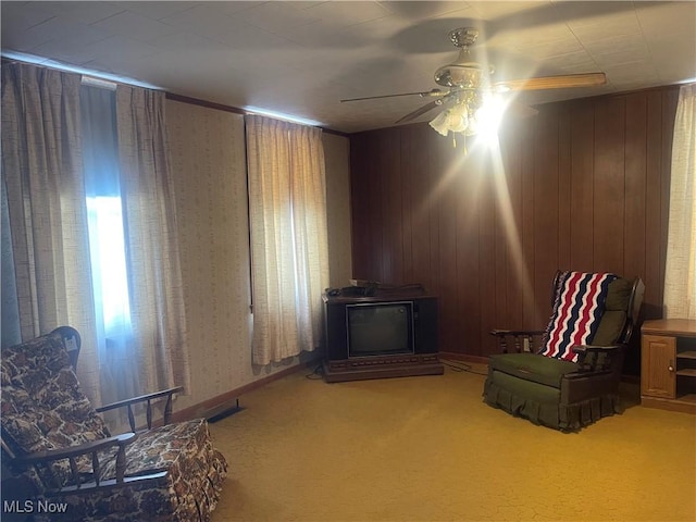 sitting room featuring carpet, a wood stove, ceiling fan, and wood walls