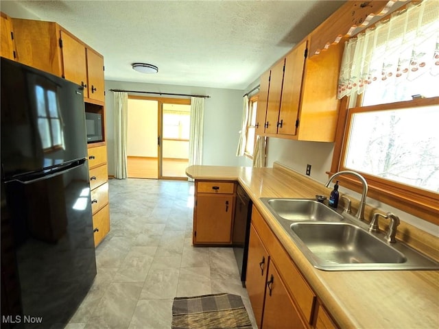 kitchen with light countertops, brown cabinets, a peninsula, black appliances, and a sink