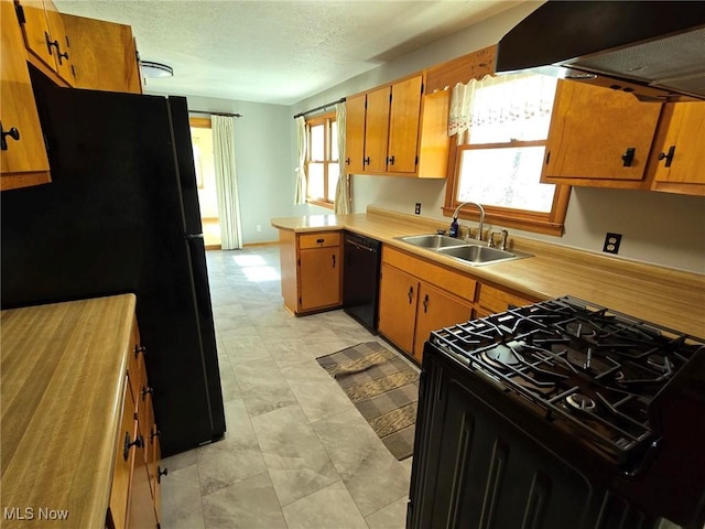 kitchen with a peninsula, a sink, black appliances, light countertops, and under cabinet range hood