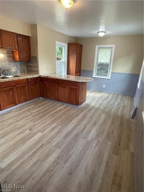 kitchen featuring kitchen peninsula, decorative backsplash, light hardwood / wood-style flooring, and sink