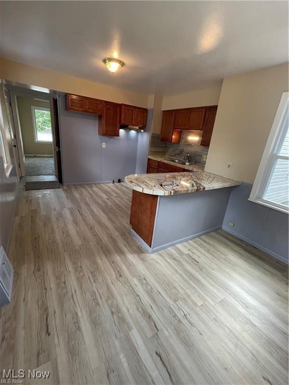 kitchen with light wood-type flooring, kitchen peninsula, sink, and tasteful backsplash