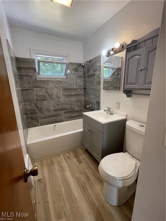 full bathroom featuring hardwood / wood-style flooring, vanity, tiled shower / bath, and a wealth of natural light